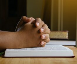 Prayer hands on a Holy Bible on wood table with window light.christian backgound