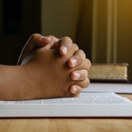 Prayer hands on a Holy Bible on wood table with window light.christian backgound